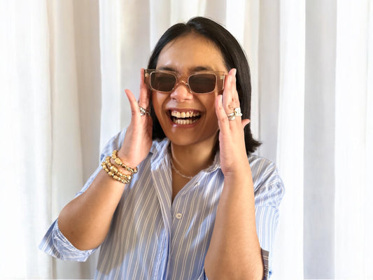 Model wearing Nina Rectangular Polarised Acetate Sunglasses in Pink, paired with a blue striped shirt and funky jewellery, posing against a neutral background