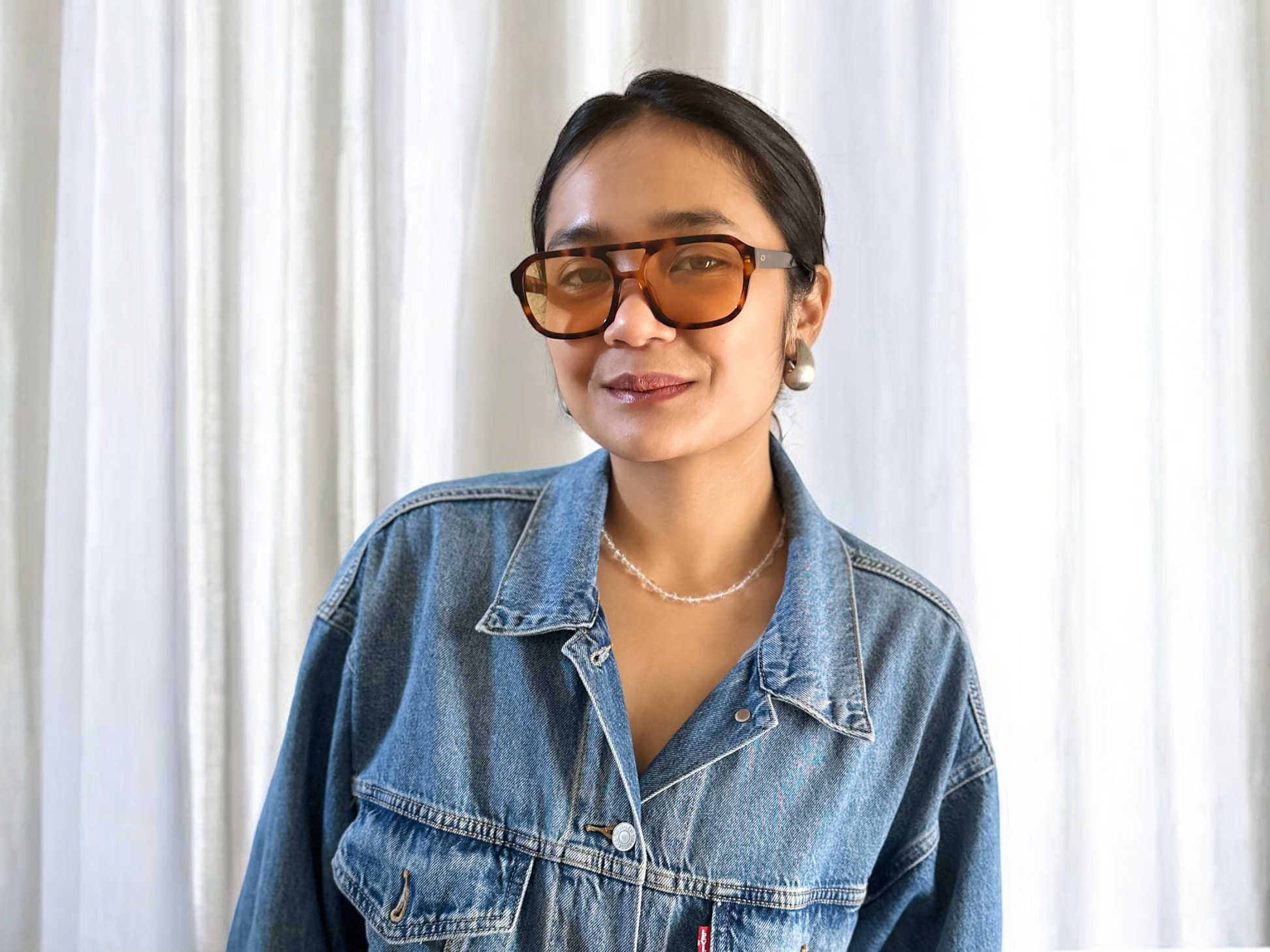 Model wearing Amber Oversized Polarised Acetate Sunglasses in Tortoiseshell with a denim jacket, standing against a white curtain backdrop